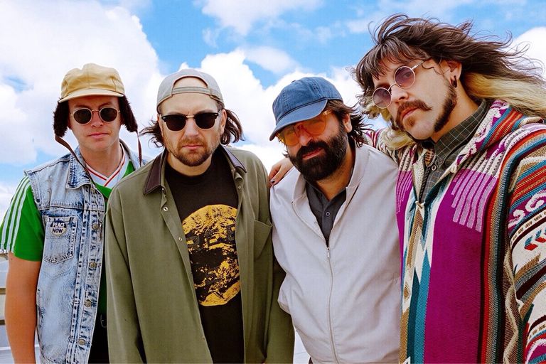 Promotional portrait of music act Real Young & Lazy Horse posing outdoors in sunglasses against a partly cloudy blue sky.